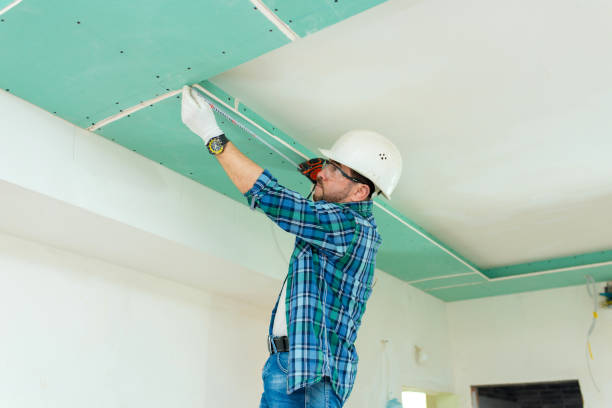 Construction worker measures plasterboard ceiling with tape measure