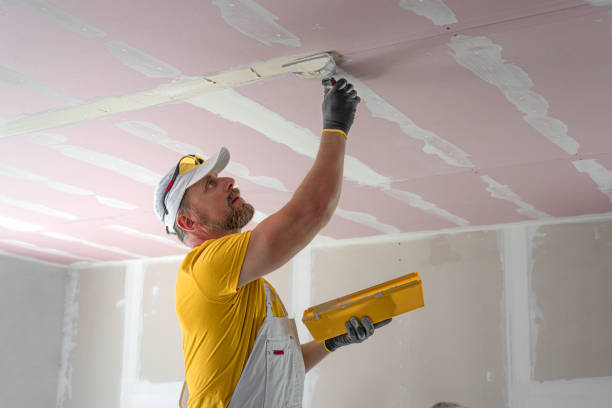 The worker make a plasterboard ceiling. He does taping plaster drywall ceiling joints. He is using special drywall taping knife.